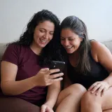 Amigas rindo de algo no celular no sofá